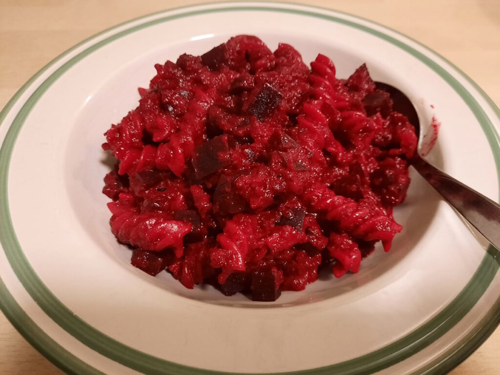 Ein tiefer Teller mit einer Portion dunkelrotem Essen. Genau genommen handelt es sich dabei um Nudeln mit Rote-Beete-Stückchen in einer Rosmarin-Rote-Beete-Sauce.
