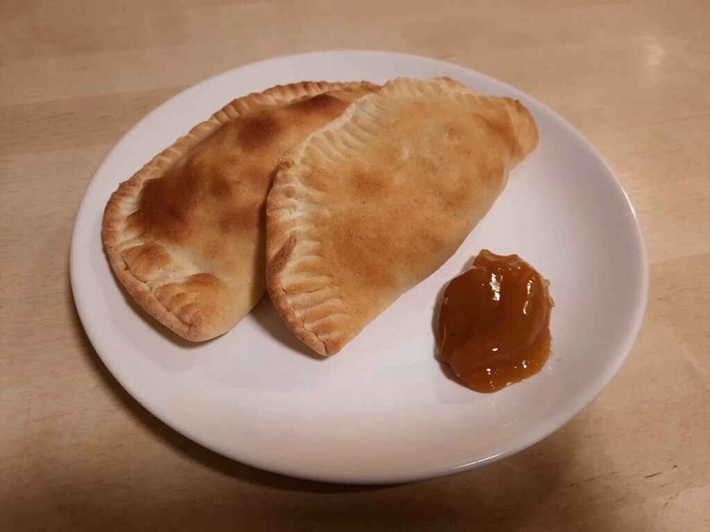 Zwei goldbraun gebackene Teigtaschen mit einem Klecks Mango-Chutney auf einem weißen Teller.