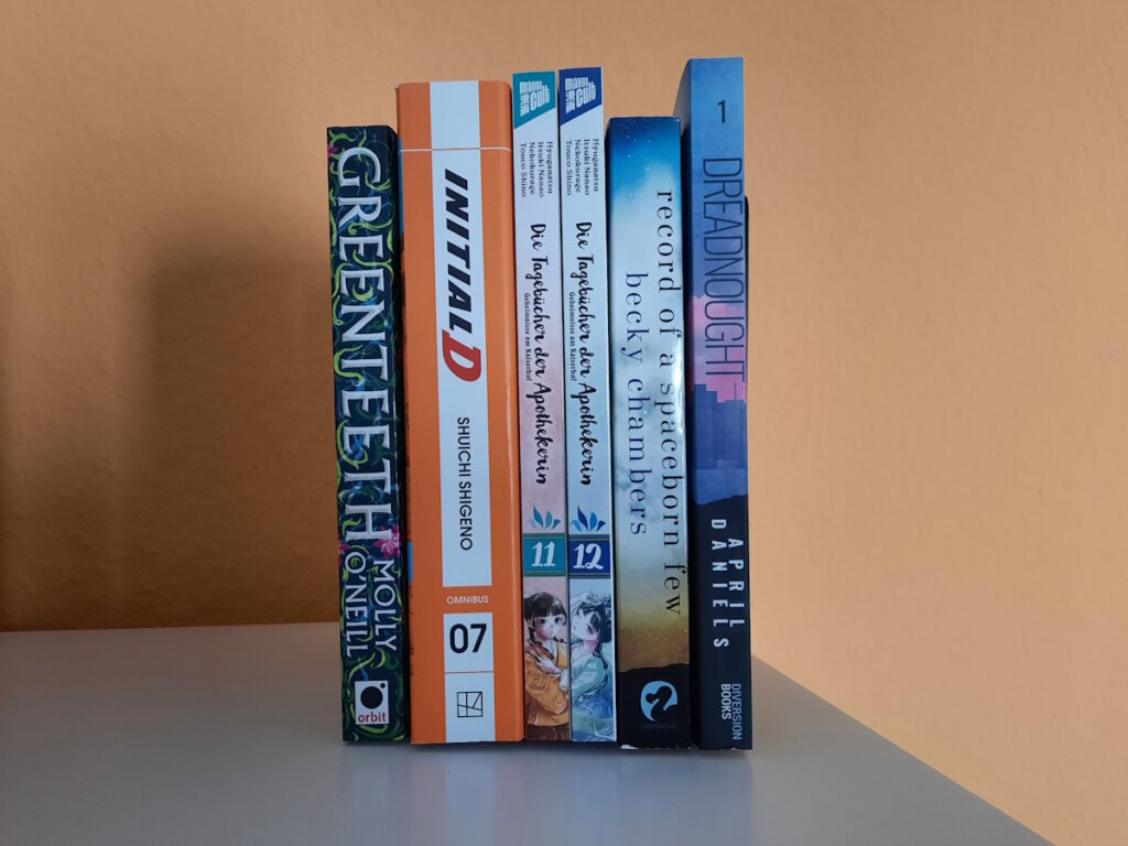 Einige Comics und Bücher zwischen zwei Buchstützen. Die Titel von links nach rechts lauten: Greenteeth von Molly O'Neill, Initial D 07 von Shuichi Shigeno, Die Tagebücher der Apothekerin 11+12, Record of Spaceborn Few von Becky Chambers und Dreadnought von April Daniels.