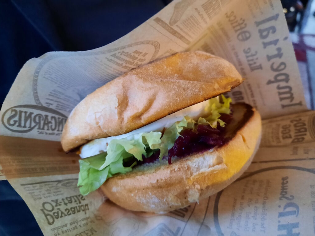 Ein Burger mit Ziegenkäse und Rotkohl in einer an Zeitungspapier erinnernden Papiertasche.