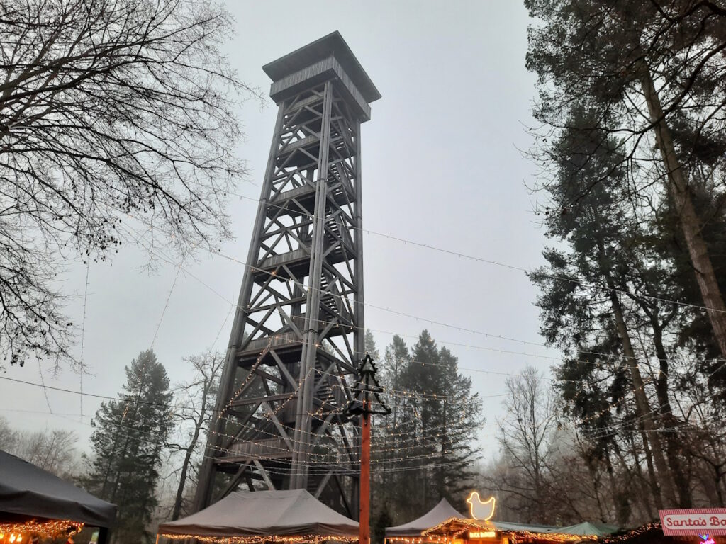 Der Frankfurter Goetheturm vor einem grauen Himmel. Darunter sind ein paar erleuchtete Buden zu erahnen.