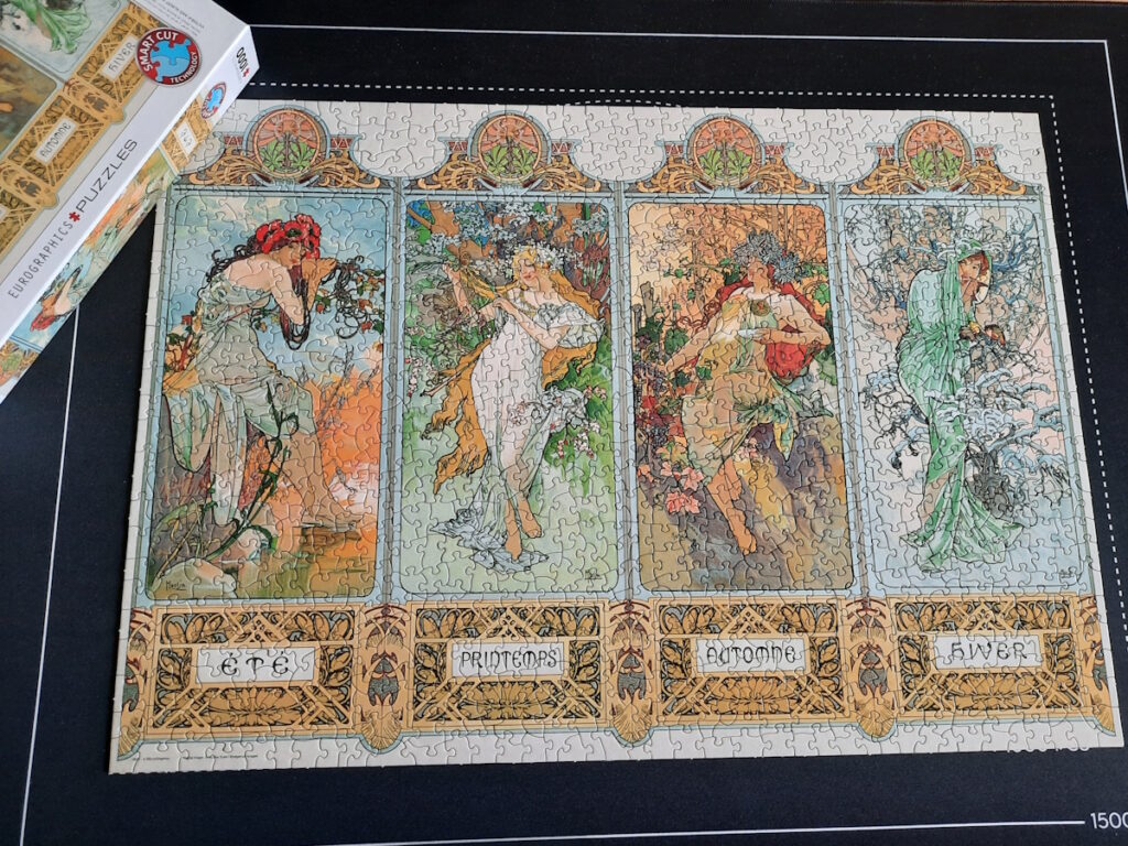 Ein fertiges Puzzle mit einem Bild von Mucha, dass vier Motive mit Frauen in je einem Rahmen zeigt. Die vier Frauen stehen dabei für die vier verschiedenen Jahreszeiten.
