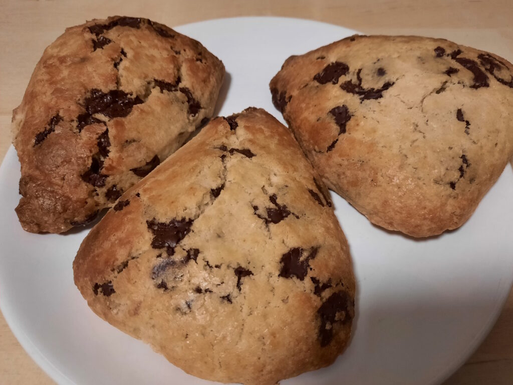 Drei goldgelb gebackene Chocolate Chip Scones auf einem weißen Teller.