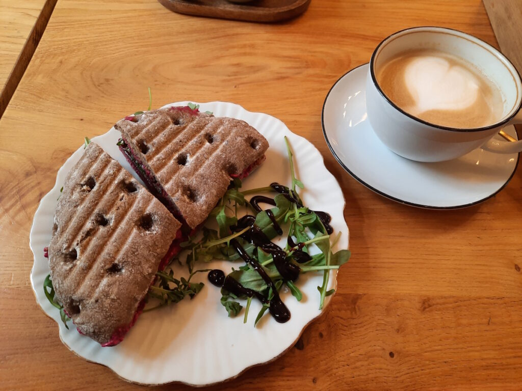 Ein Cafétisch mit einem Teller mit einem Panini und einer Tasse Milchkaffee.