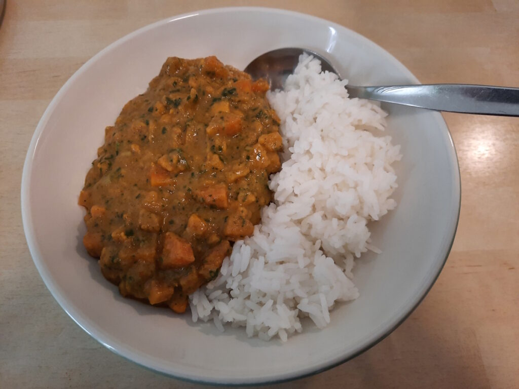 Eine Schale, die zur Hälfte (rechts) mit Reis und zur Hälfte (links) mit Süßkartoffel-Curry gefüllt ist.