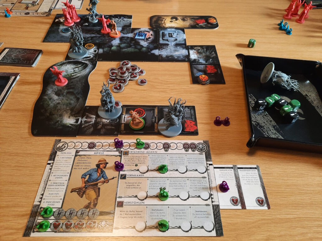 Eine Runde des Brettspiels "Death May Die". Im Vordergrund ist das Charakterblatt der Jägerin Ariele zu sehen. Rechts neben dem Spielbrett ist eine Würfelschale mit sieben Würfeln, von denen sechs einen Erfolg zeigen.
