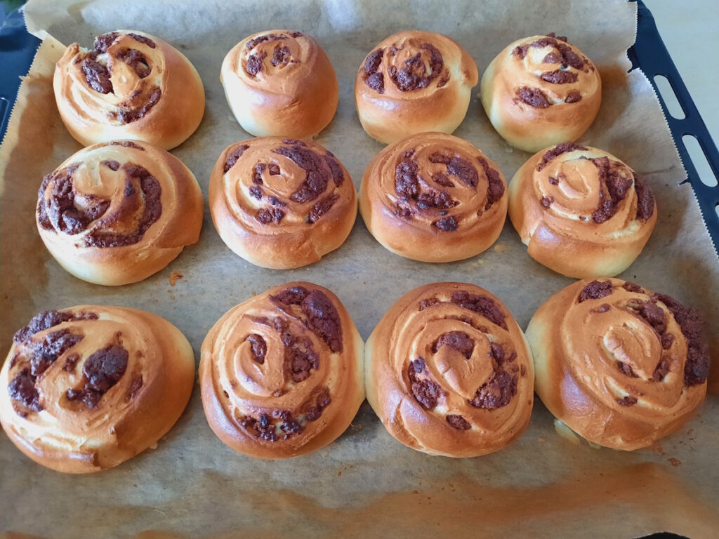 Zwölf frisch gebackene goldbraune Hefeschnecken mit einer Schoko-Marzipan-Füllung auf einem Backblech.