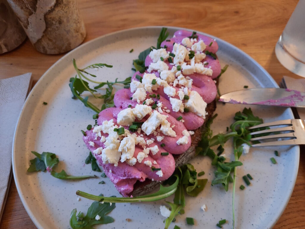Ein Brot mit Rote-Beete-Creme und gebröseltem weißem Käse. Daneben lässt sich ein Glas mit Limonade erahnen.