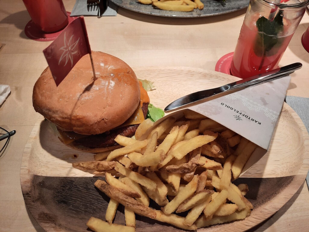 Ein großer Holzteller mit einem Burger und einer großen Tüte goldbrauner Pommes.