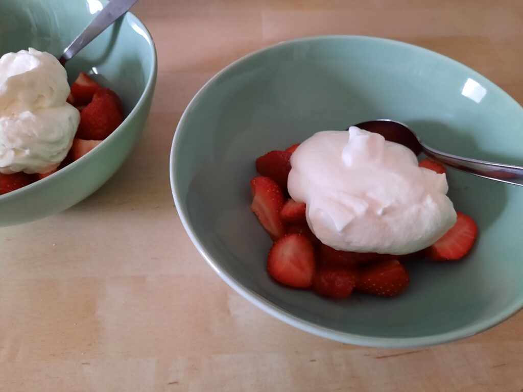 Eine zartgrüne Schale mit einer Portion frischer Erdbeeren und Sahne.