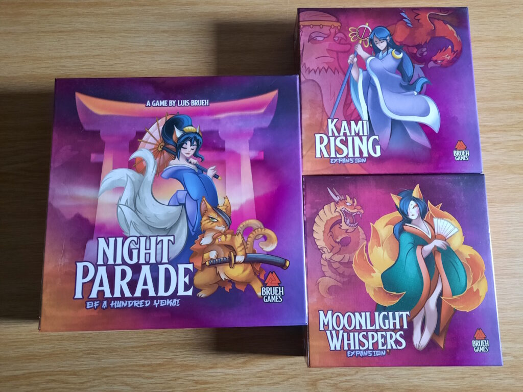 Die Schachtel des Brettspiels Night Parade und zwei Schachteln mit Erweiterungen (Kami Rising und Moonlight Whispers)