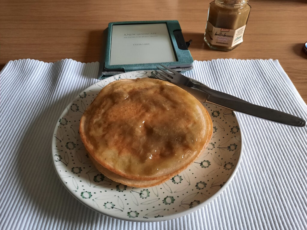 Ein Teller mit Pancakes, die mit Rharbarber-Vanille-Kompott. Im Hintergrund ist ein angeschalteter eReader zu sehen.