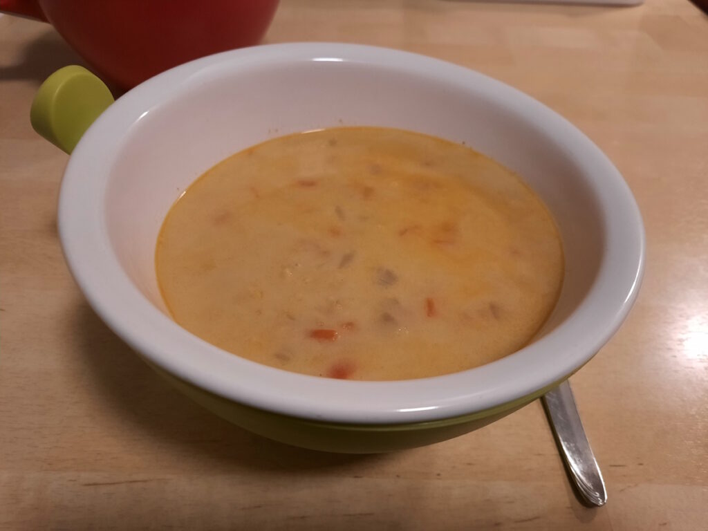 Eine gelbe Suppe mit einigen appetitlich aussschauenden Paprikastücken in einer Schale.