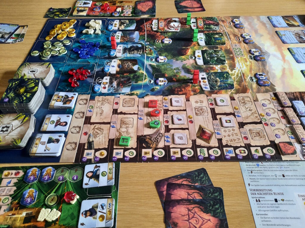 Der Aufbau einer Runde "Die verlorenen Ruinen von Arnak" mit dem Vogeltempel. Das Spielbrett ist voller kleinteiliger Elemente wie Orte, die erkundet werden können, Items wie Geld, Rubine oder Pfeilspitzen und im Vordergrund ist der Tempelbereich in dem Forschung betrieben wird.