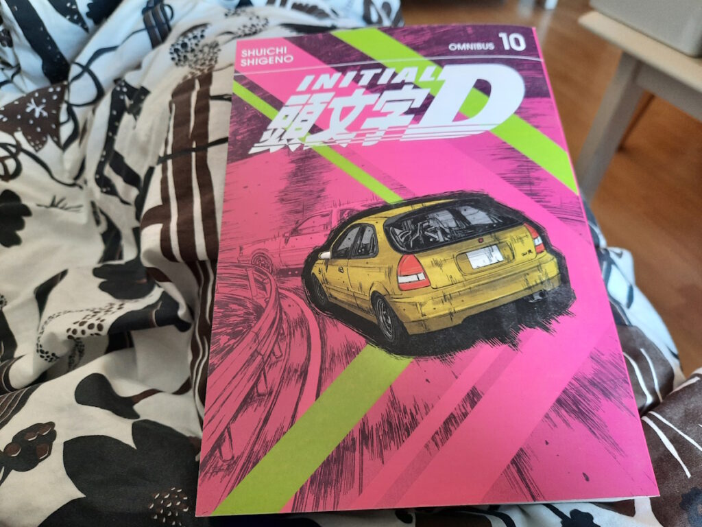 Der zehnte Band der Omnibus-Ausgabe von Initial D. Das pinke Cover zeigt einen gelben Sportwagen schnell durch eine Kurve fahren. Darüber steht der Titel der Mangareihe auf Englisch und auf Japanisch.