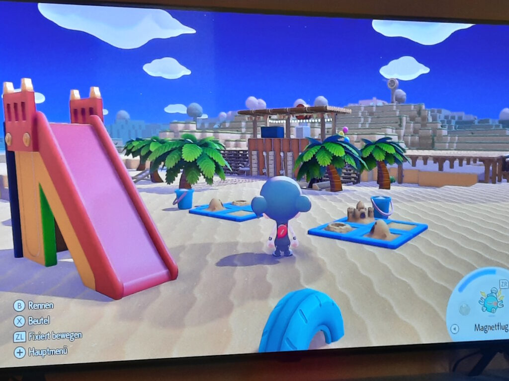 Ein Pokopia-Screenshot, bei dem meine Figur zwischen einer Rutsche und zwei Sandkästen steht und auf einen palmenbewachsenen Strandbereich schaut. Im Hintergrund ist eine Holzkonstruktion mit ein paar Duschen zu erahnen.