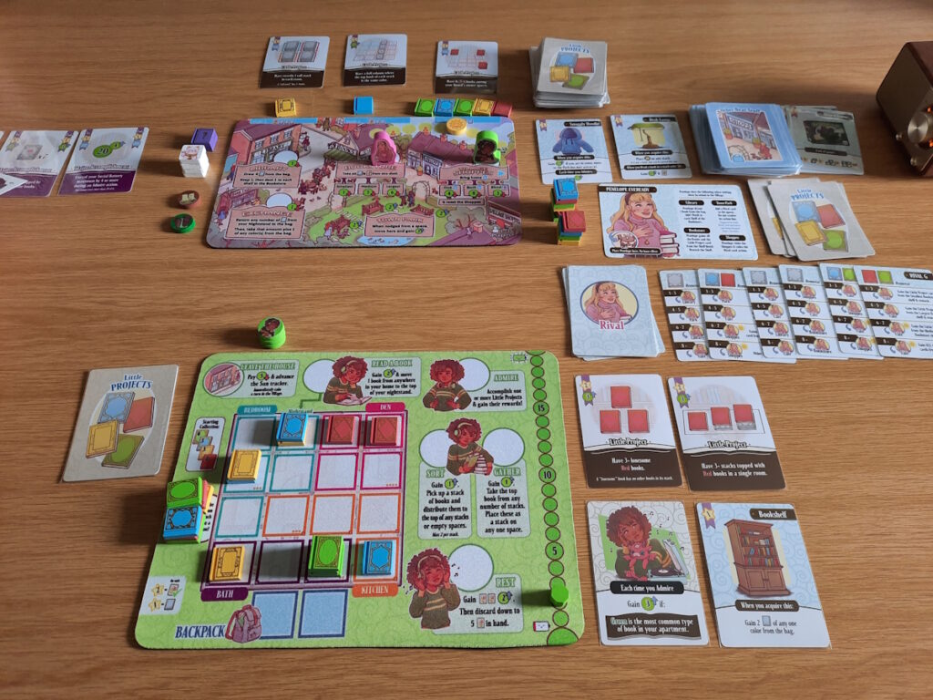 Der Aufbau einer Solo-Spielrunde des Brettspiels "A Place for All My Books". Es ist ein Playerboard zu sehen, das ein Apartment mit verschiedenen Orten sein soll, und Hinweisen mit den verschiedenen Tätigkeiten, die mit den Büchern durchgeführt werden können. Im Hintergrund ist ein Brett mit einer Ortsmitte zu sehen und daneben die Karten, die für meine "Gegenspielerin" stehen.