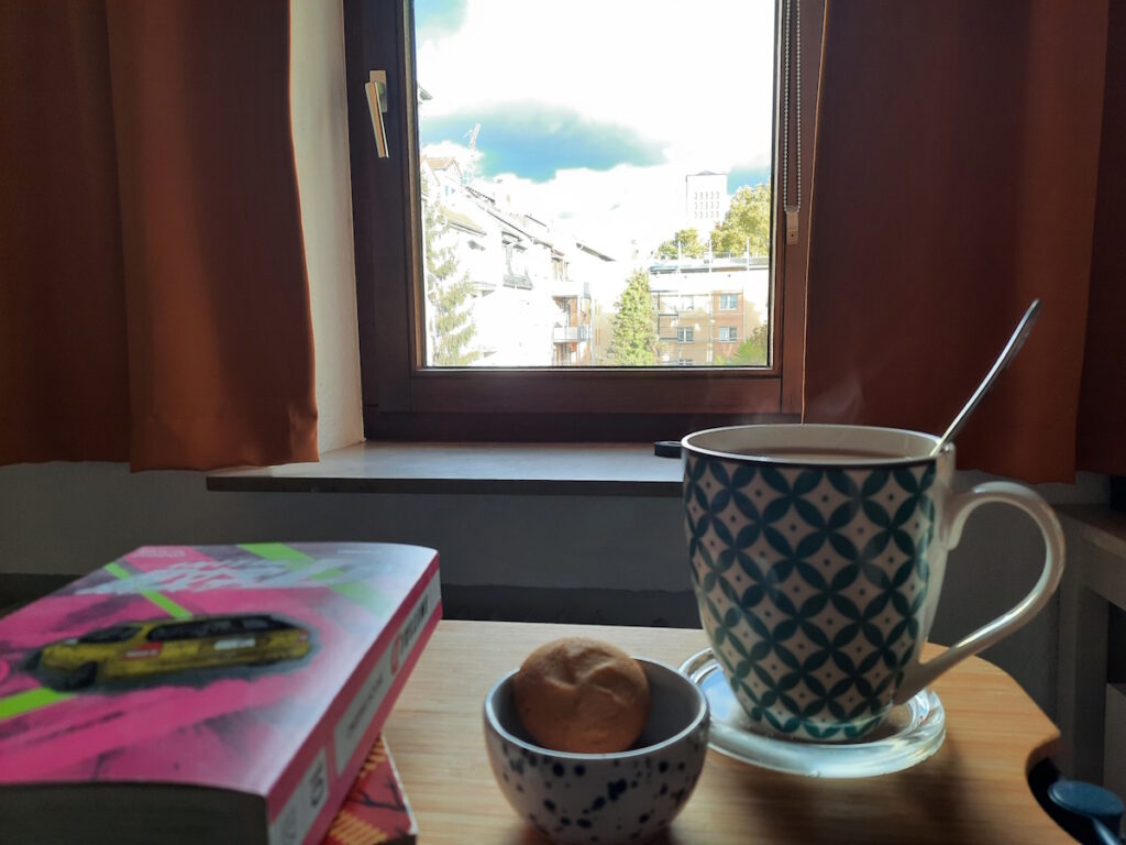 Ein kleines Schälchen mit zwei Zitronenkeksen und eine große Tasse mit dampfendem Tee.